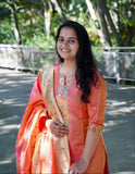 Woman in an orange traditional outfit standing outdoors with greenery in the background